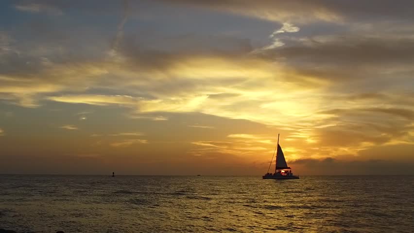 Watching the ocean waves crash ashore as the sailboat crosses a beautiful sunset at the southern most point of Key West Florida in high quality slow motion