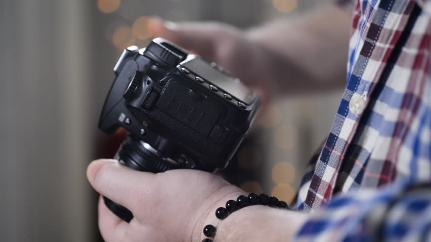 A man in a plaid shirt with a bracelet on his hand using a DSLR camera.