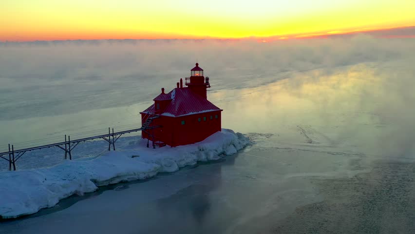 Stunning lonely lighthouse amid snow, ice and steaming foggy waters, aerial view.
