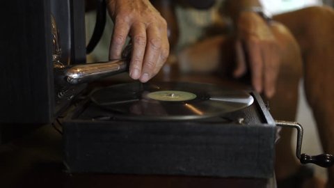 Hand of old man plays vintage records on antique gramophone.