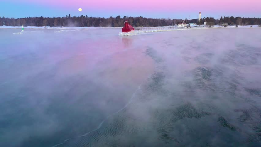Stunning lighthouse with full moon in steaming foggy waters, aerial view.
