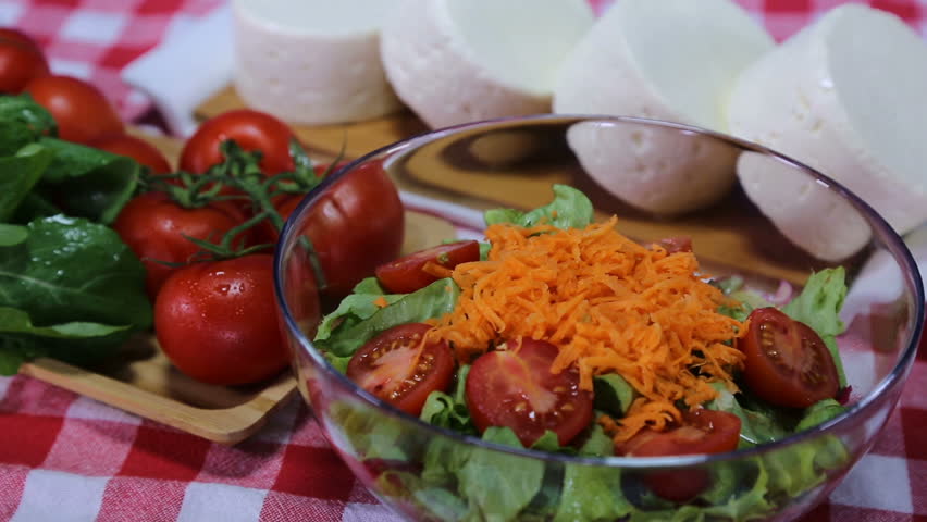 Big bowl of salad with carrots and cheese, season salad on red white scotch tablecloth, dropping cheese on salad, vegeterian food, feta cheese