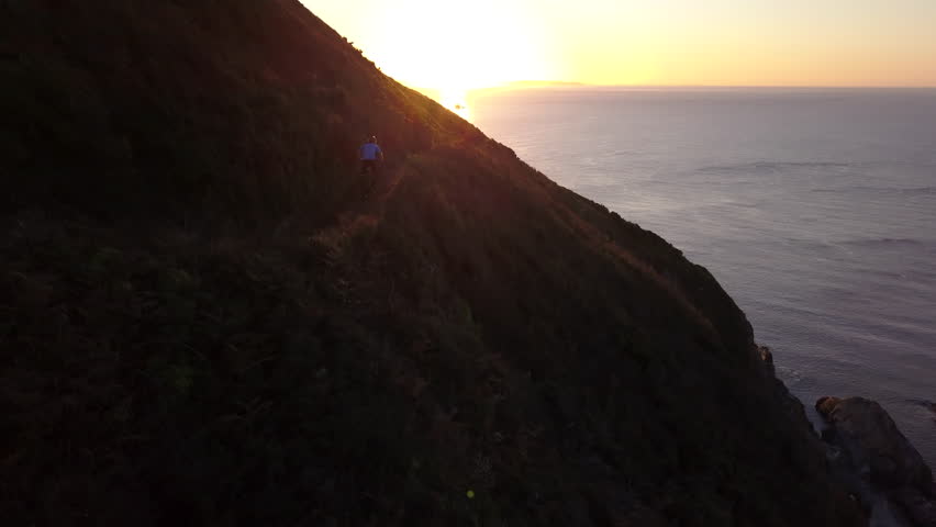 A Mountain biker riding quickly downhill on a cliff path with a view of the sea on a sunny morning