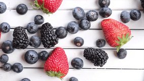 Mix strawberry, blueberry and blackberry fruits on wooden board. Selective focus. Top view tracking shot.