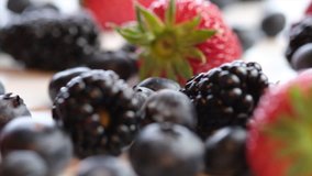 Mix strawberry, blueberry and blackberry fruits on wooden board. Selective focus. Tracking shot.