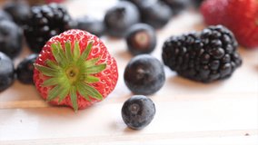 Mix strawberry, blueberry and blackberry fruits on wooden board. Selective focus. Tracking shot.