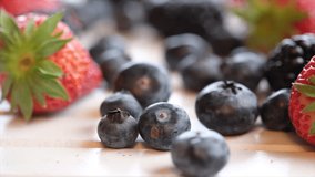 Mix strawberry, blueberry and blackberry fruits on wooden board. Selective focus. Panning to the right.