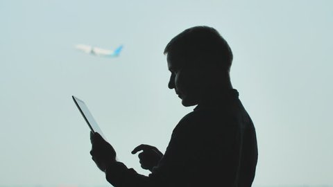 Silhouette of young men using tablet pc on the background of an airplane taking off.
