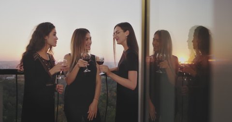 Three charismatic ladies in the top of building at the balcony drinking wine and chatting with each other