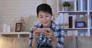 Confused young woman sitting alone on couch in living room at home at night looking at smartphone screen with irritation and indignant. Annoyed lady with error cellphone while watching series online