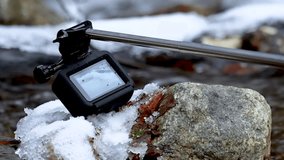 Action can on selfie stick taking close up video of ice covered stone on fast flowing creek waters.