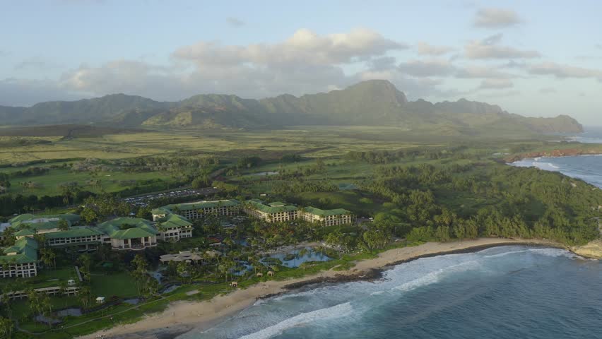 Keoniloa Bay Poipu Kauai aerial drone shot of coastline, beach and resort distant mountain. Shipwreck beach in Hawaii. Rolling waves and blue ocean