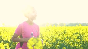 4K video clip of beautiful healthy mixed race African American girl teenager female young woman drinking from water bottle and running or jogging in field of yellow flowers