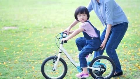Asian family with Mother teaches her daughter or children Girl to ride a bicycle having fun in nature or park and sunlight. Slow Motion