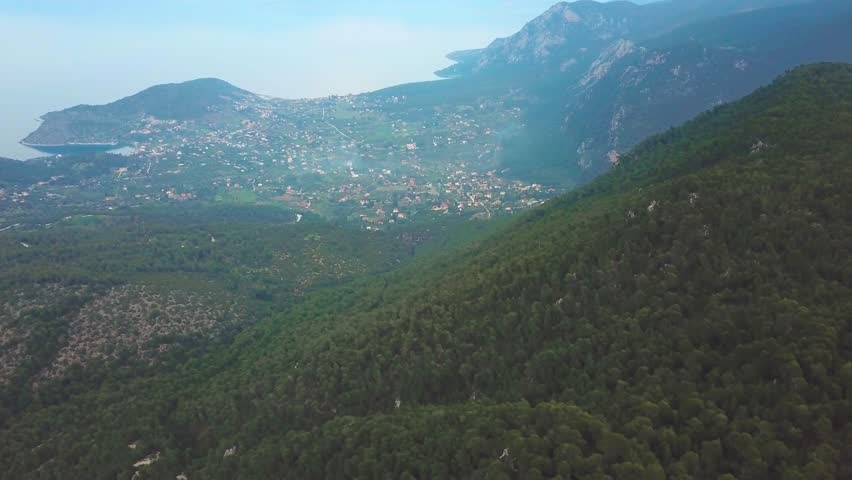 Drone shot while landing of a pine tree forest and in the bachground a village next to the sea during blue hour in Greece