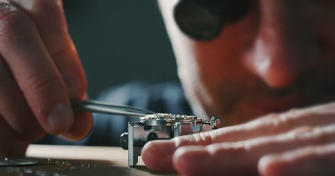 Slow motion close up of a professional watchmaker repairer working on a luxury mechanism watch gears in a workshop. Shot in 8K.