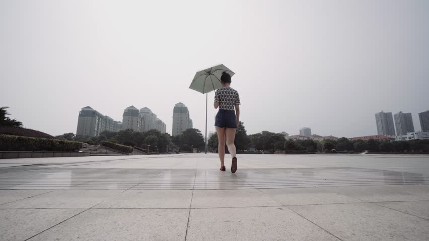 Pretty Chinese girl walking under her sunshade on an concrete esplanade in China