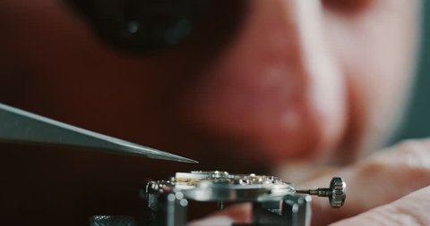 Slow motion close up of a professional watchmaker repairer working on a luxury mechanism watch gears in a workshop. Shot in 8K.