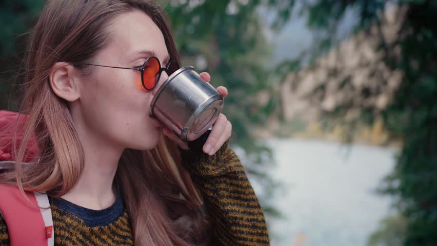 Girl traveler rest and relax stop after hiking walking pouring and drinking hot tea or liquid beverage from thermos and enjoying the taste in beautiful nature place in pine woods forest mountain lake | Shutterstock HD Video #1025138765