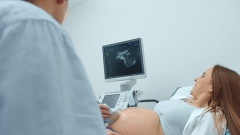 Doctor woman performing an ultrasound procedure on pregnant beautiful woman.