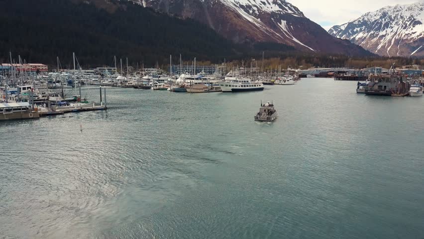 Following boat in beautiful Seward small boat harbor, snow on distant mountains. Alaska 4k.