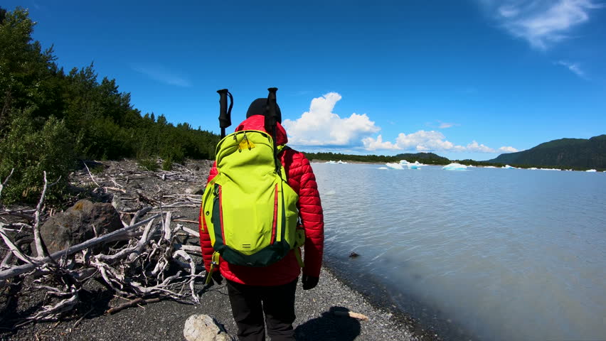 POV of ambitious female hiker walking passed driftwood along the Pacific Northwest shoreline melting icebergs floating on glacial waters USA