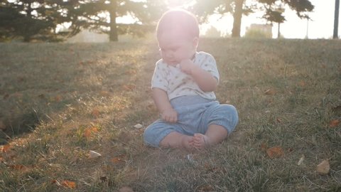 Small baby girl sitting on grass in park. Beautiful baby portrait in nature