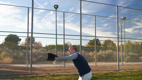 An athlete baseball player catching and throwing a ball to a teammate in slow motion on a grass park field during spring training.