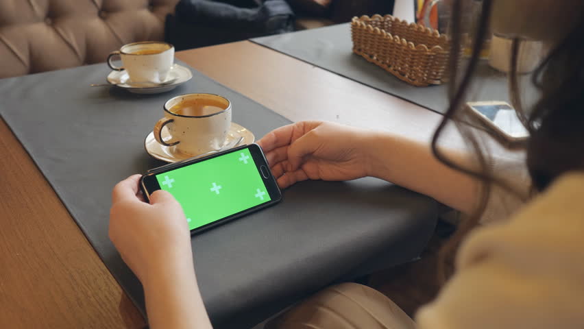 woman using mobile cell phone with green touch screen in cafe, back view