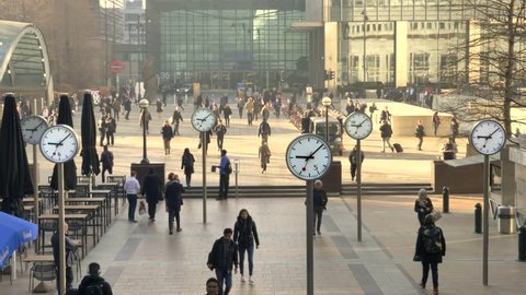 London, England - February 28, 2019: Business Men and women at Canary Wharf durning morning rush hour, with large analog clocks spinning fast, Time and business concept.