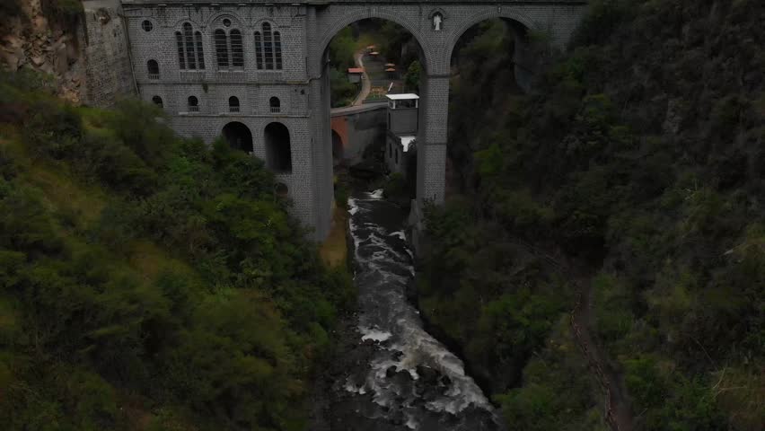 River flows under a gothic style church as tourists walk around in southern Colombia