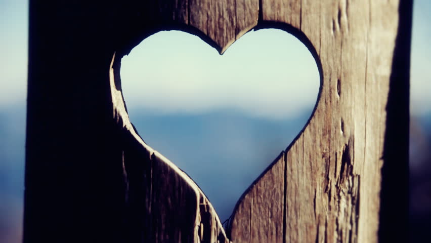 Rack focus handheld shot: from the shape of a heart carved in a wooden stake, to a breathtaking panorama of snowy mountains in winter. Symbolic meaning: love for the nature.