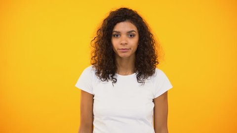 Afro-american female shrugging shoulders, unsure of choice, yellow background
