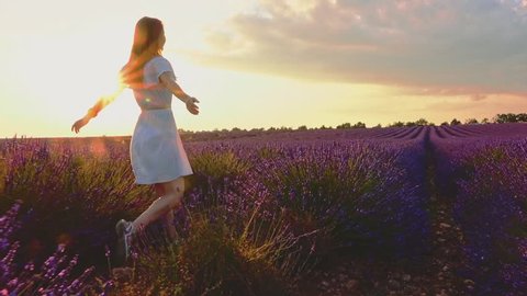 Happy Woman Enjoying Life in Lavender Field at Sunset. SLOW MOTION 120 FPS STABILIZED SHOT. Joyful girl walking in endless blooming lavender fields. Plateau du Valensole, Provence, France. Lens Flare