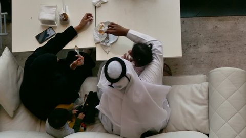 Top view of an Arab family sitting on a sofa eating dessert 
