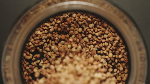 TOP VIEW: Brown lentils grains pouring into a glass jar - Slow Motion