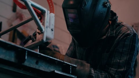 Man welds in garage wearing welding mask sparks cascading