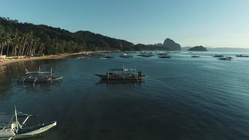 Aerial drone view of boats anchored in the bay with clear and turquoise water on the sunset. Boat and yacht in the tropical lagoon. Tropical landscape. El Nido, Palawan island, Philippines.