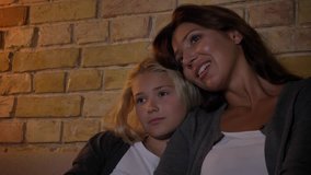 Closeup shoot of young caucasian mother and a girl watching TV while sitting on sofa and hugging. Mom talking to her daughter with affection