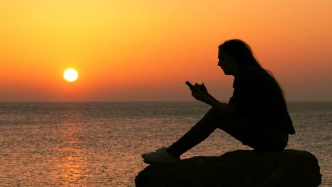 Side view portrait of a sad girl silhouette complaining checking smart phone at sunset on the beach