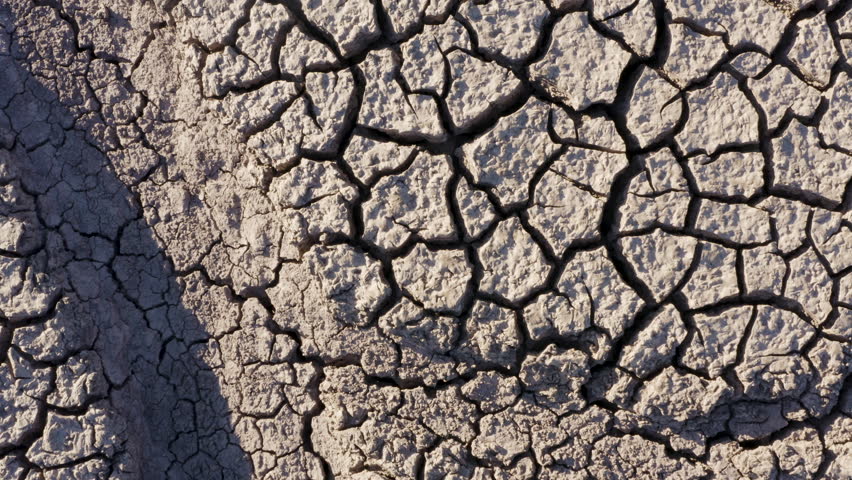 Climate change.High aerial zoom out view of a devastated farmer walking across the patterned cracked mud surface of a dry dam due to drought from climate change and global warming Royalty-Free Stock Footage #1025199995