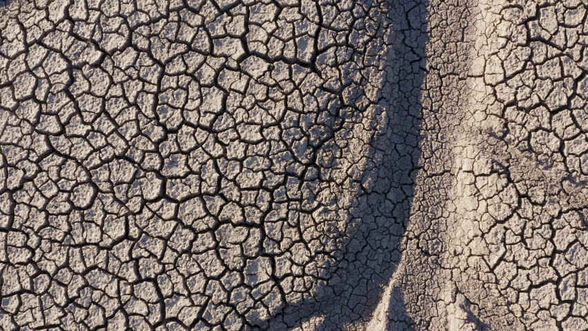 Climate change.Aerial zoom out view of a devastated farmer walking across the patterned cracked mud surface of a dry dam due to drought from climate change and global warming Royalty-Free Stock Footage #1025200034