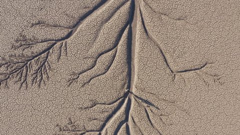 Climate change.Aerial zoom out view of a devastated farmer walking across the patterned cracked mud surface of a dry dam due to drought from climate change and global warming