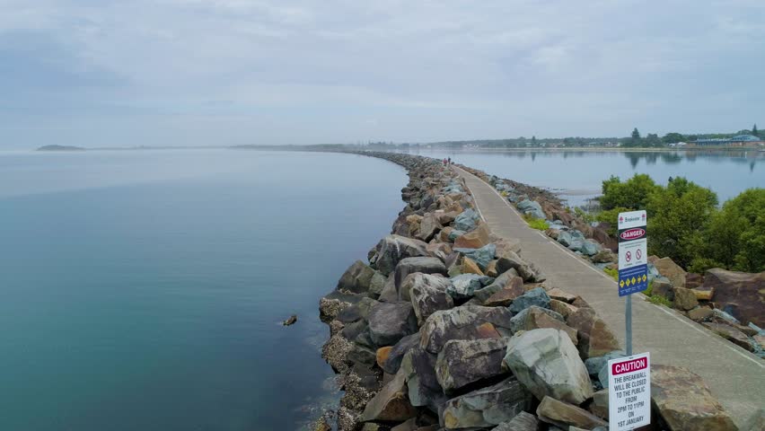 Aerial rise above scenic long breakwall revealing river and ocean. Harrington, New South Wales, Australia