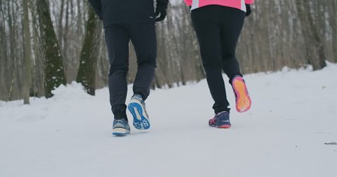 Close-up of the feet of two runners in sneakers running in the winter in the park. The married couple goes in for sports.