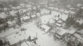 Aerial drone footage following snowy suburban roads in the middle of a snow storm.  Snowflakes and blowing snow visible in the video.