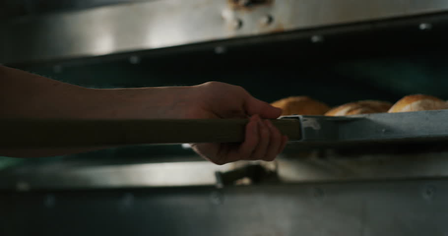 Slow motion close up of a baker pulling out from the oven warm fresh bread just made in a bakery. | Shutterstock HD Video #1025207198