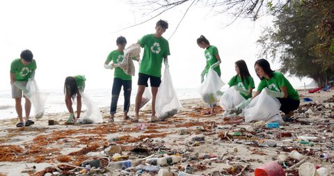 Group of asian people cleaning up the beach with plastic bags full of garbage. People with environment and volunteering concept. 4k resolution.