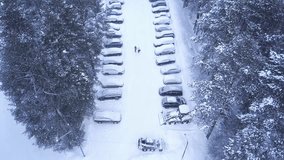 Top view of winter parking in forest. Clip. Snow-covered car park with people walking in middle of road in forest in winter