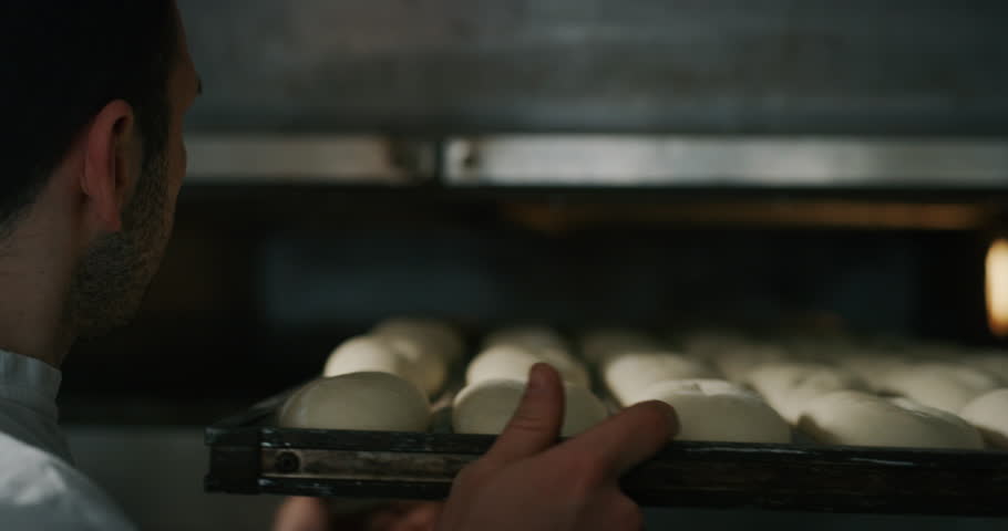 Slow motion close up of a baker pulling into the oven balls of dough covered with wheat flour ready for baking in bakery. Royalty-Free Stock Footage #1025221292